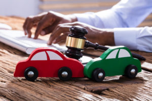Two Wooden Cars With Judge Mallet And Gavel On The Businessman's Desk Using Keyboard