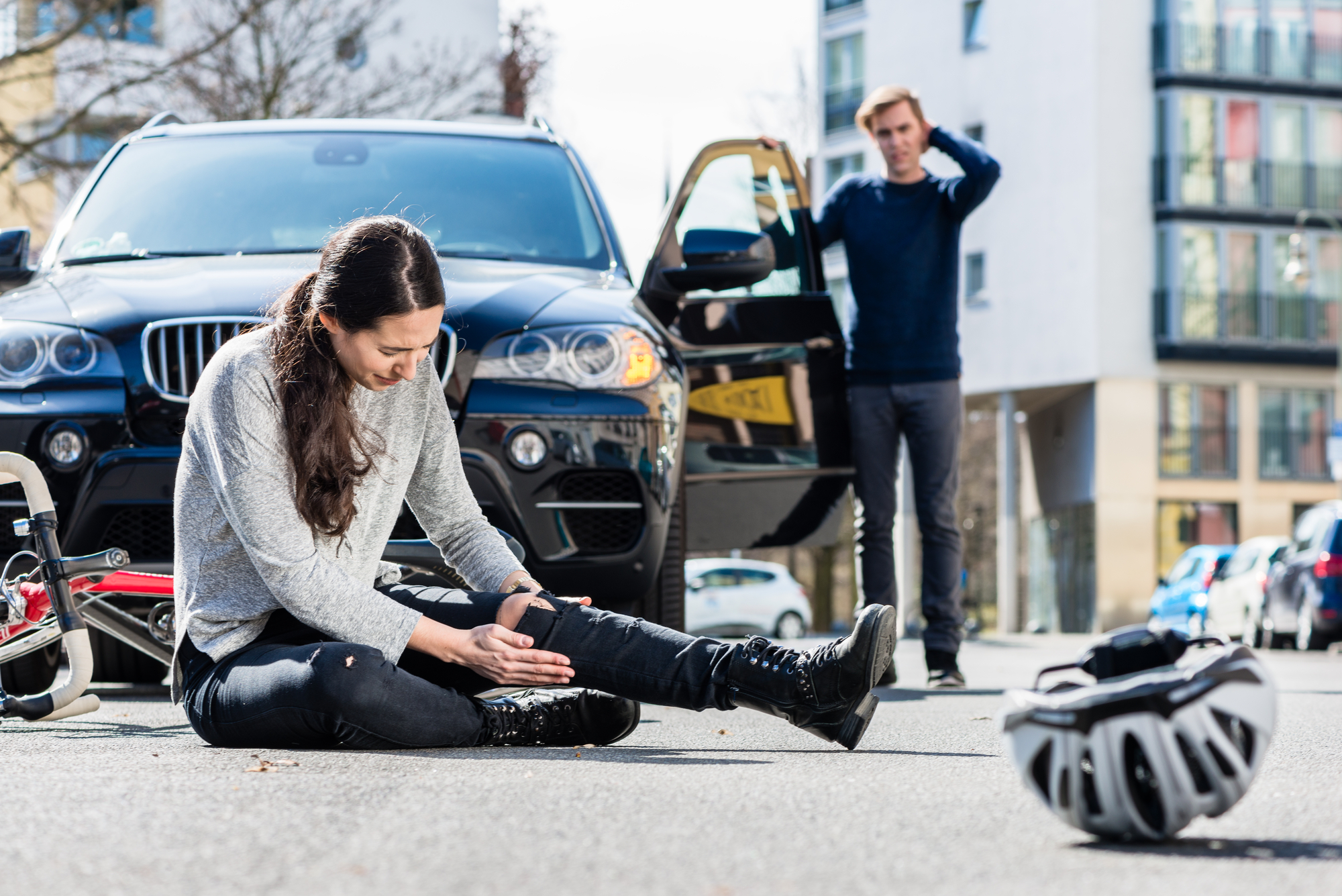 What To Do After a Bike Accident - Full length of a young female bicyclist fallen down on street with serious injuries after traffic accident with the 4x4 car of a young man